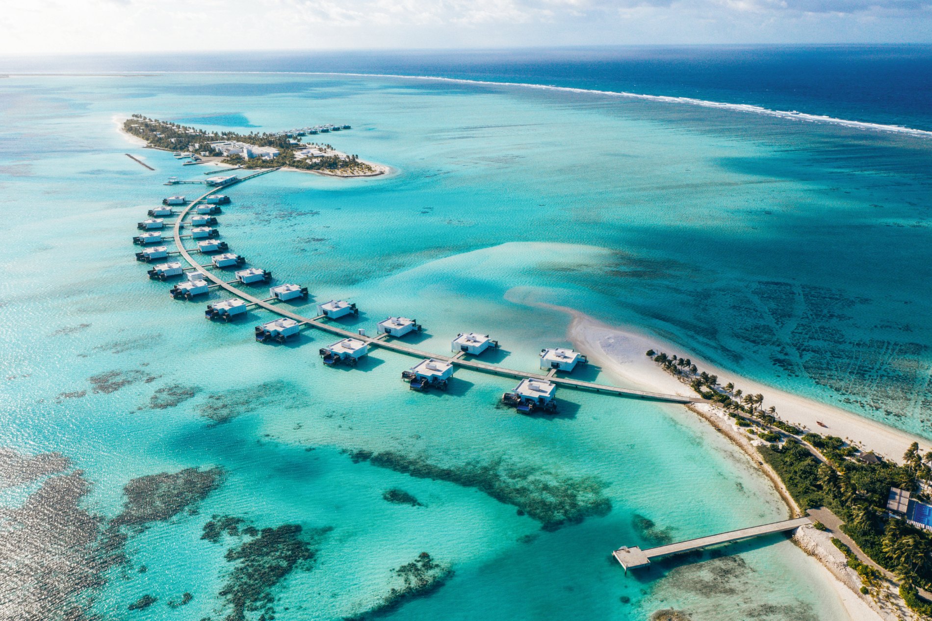 Une île-hôtel des Maldives vue du ciel, ses villas sur pilotis et son lagon
